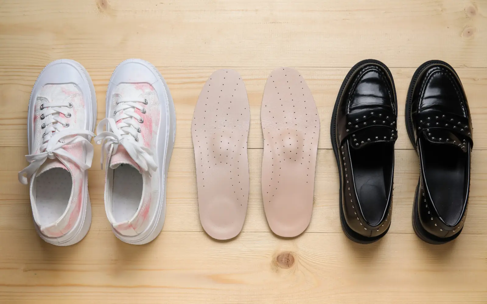 Trainers, a pair of arch-support insoles and dress shoes laid out on pale wood for comparison.