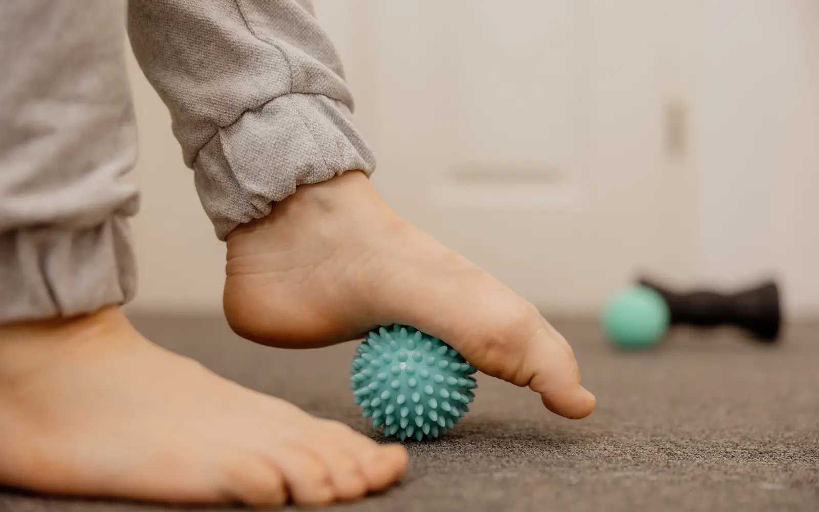 A bare foot rolling a spiked massage ball along the arch, one of the self-treatments for plantar fasciitis.